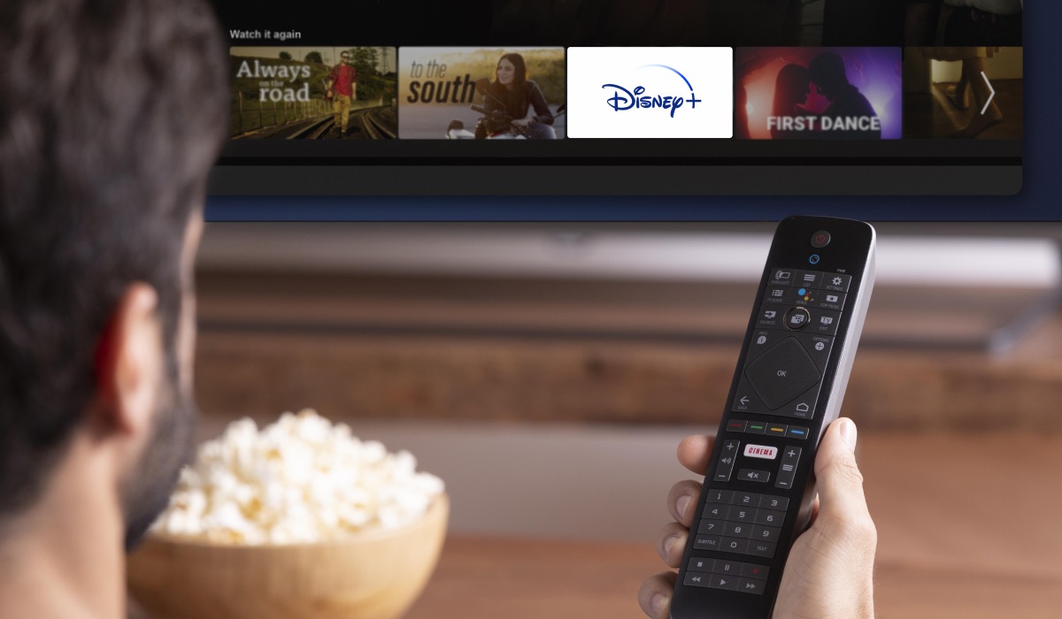 A person holding a remote and a bowl of popcorn. A Smart TV with Disney Plus icon on the interface